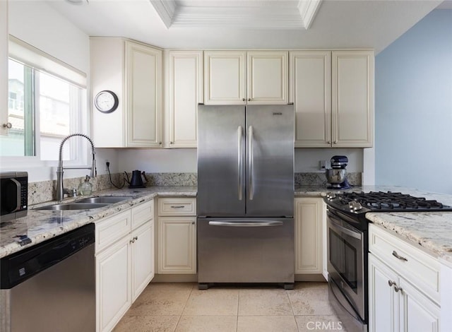 kitchen with crown molding, appliances with stainless steel finishes, cream cabinets, a raised ceiling, and a sink