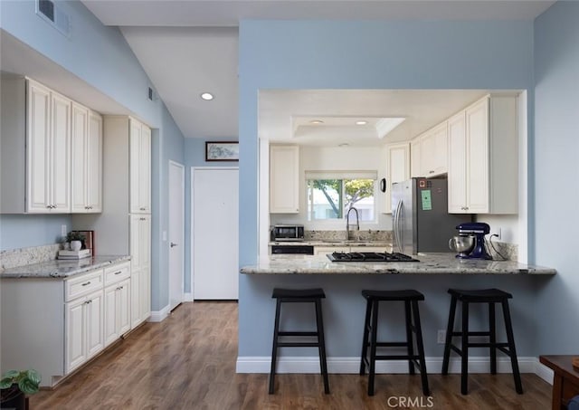 kitchen featuring a kitchen bar, a peninsula, light stone countertops, and freestanding refrigerator