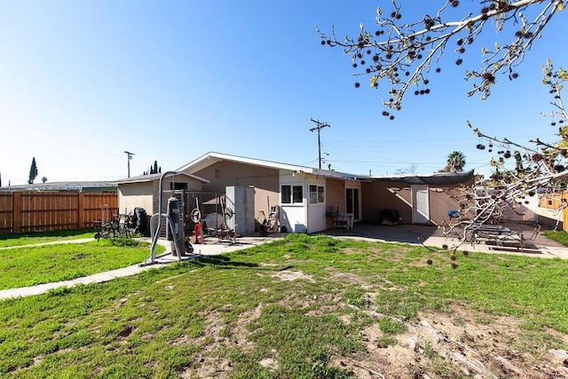 rear view of house with a yard, a patio, stucco siding, and fence