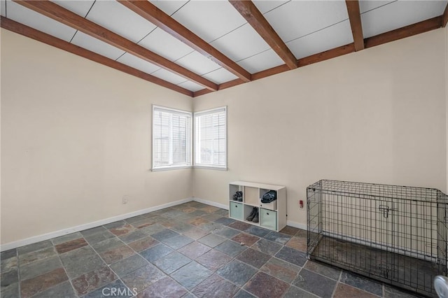 unfurnished room with baseboards, beam ceiling, and stone tile flooring