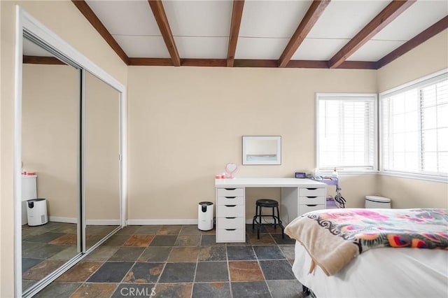 bedroom with beam ceiling, a closet, stone finish flooring, and baseboards