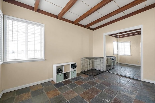 spare room with baseboards, stone tile floors, and vaulted ceiling with beams