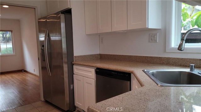 kitchen with a sink, stainless steel appliances, white cabinets, light tile patterned flooring, and light stone countertops