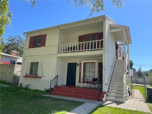 view of front of property featuring fence, stairway, a front yard, a balcony, and a gate