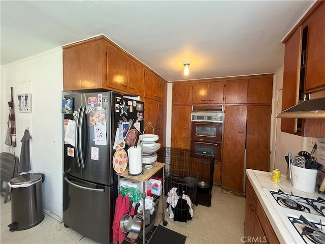 kitchen with tile countertops, double wall oven, freestanding refrigerator, white gas stovetop, and brown cabinets