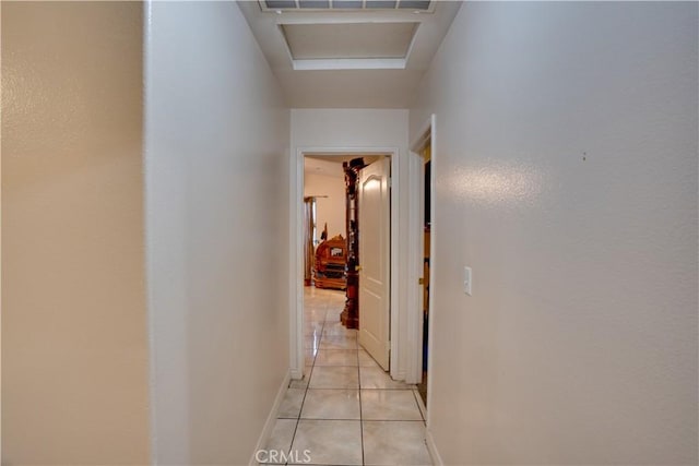 hall with light tile patterned floors, attic access, and baseboards