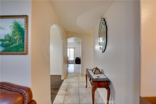 hallway featuring light tile patterned floors, baseboards, lofted ceiling, arched walkways, and light carpet