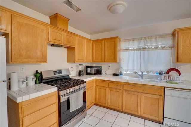 kitchen featuring tile countertops, a sink, black microwave, stainless steel gas range oven, and dishwasher