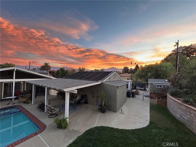 back of house at dusk featuring a patio, a fenced in pool, an outbuilding, and roof with shingles