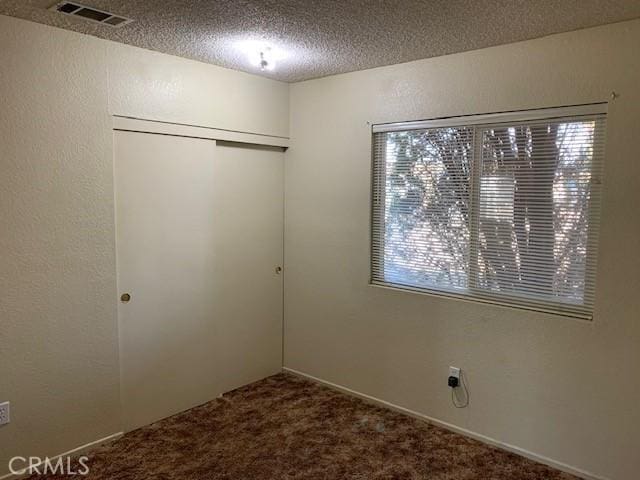 unfurnished bedroom with visible vents, carpet floors, a closet, a textured ceiling, and a textured wall