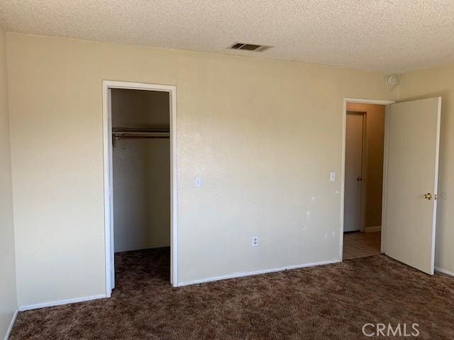 unfurnished bedroom featuring a walk in closet, carpet flooring, visible vents, and a textured ceiling