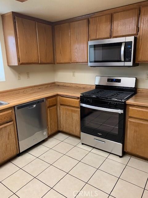 kitchen with light tile patterned floors, stainless steel appliances, brown cabinetry, and light countertops