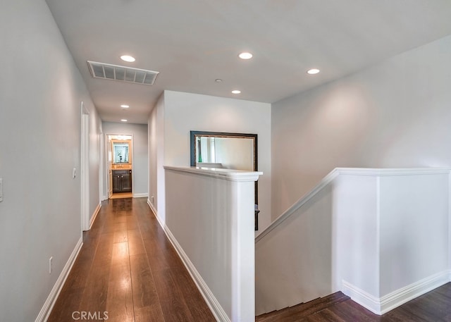 hallway with visible vents, baseboards, recessed lighting, dark wood-style flooring, and an upstairs landing