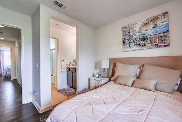 bedroom with visible vents, connected bathroom, baseboards, and wood finished floors