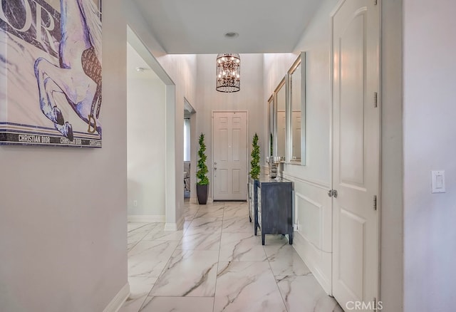 hallway featuring a chandelier, marble finish floor, and baseboards