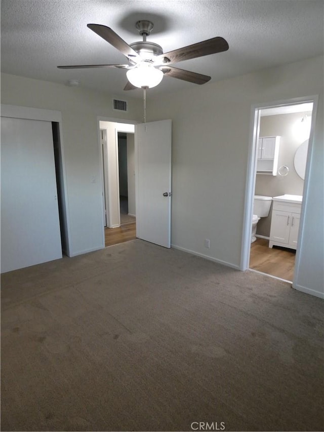 unfurnished bedroom with visible vents, ensuite bathroom, a textured ceiling, carpet, and ceiling fan