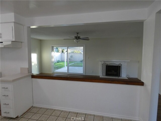 interior space featuring a brick fireplace, ceiling fan, under cabinet range hood, light tile patterned floors, and white cabinetry