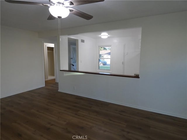 empty room with dark wood finished floors, visible vents, a ceiling fan, and baseboards