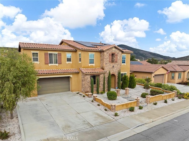 mediterranean / spanish home featuring stucco siding, driveway, stone siding, a garage, and solar panels