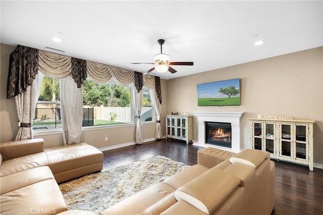 living area with a glass covered fireplace, visible vents, baseboards, and wood finished floors