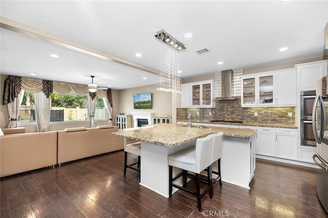 kitchen with visible vents, backsplash, dark wood-style floors, wall chimney exhaust hood, and white cabinets