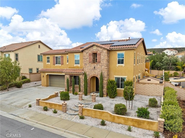 mediterranean / spanish home featuring stucco siding, driveway, stone siding, roof mounted solar panels, and fence