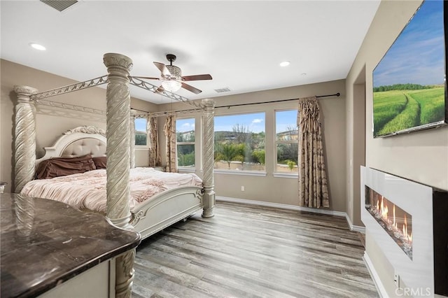 bedroom with visible vents, a warm lit fireplace, wood finished floors, recessed lighting, and baseboards