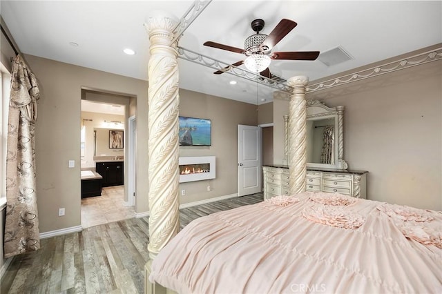 bedroom with wood finished floors, baseboards, visible vents, a lit fireplace, and connected bathroom