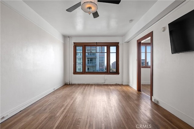 empty room featuring wood finished floors, baseboards, and ceiling fan