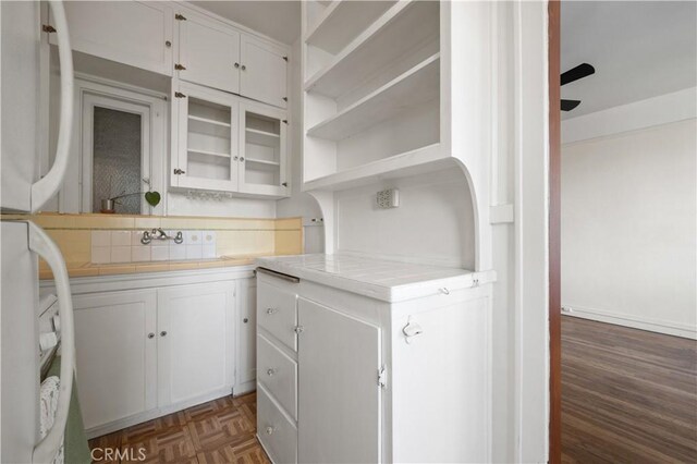 kitchen featuring tile countertops, backsplash, white cabinets, and a sink