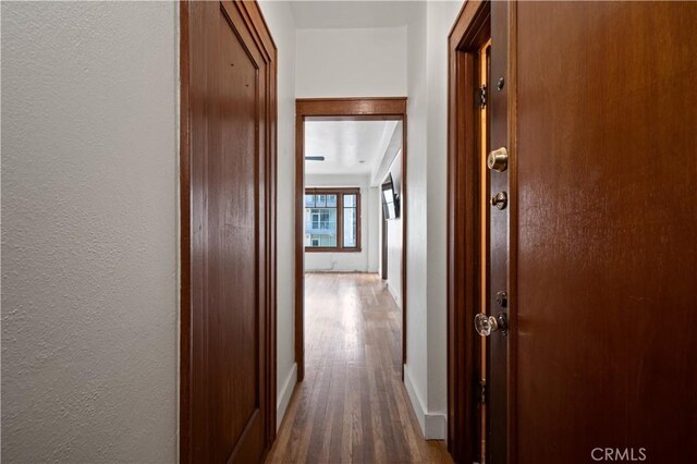 hallway with a textured wall, baseboards, and wood finished floors