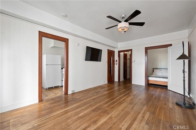 unfurnished bedroom featuring hardwood / wood-style flooring, a ceiling fan, baseboards, and freestanding refrigerator