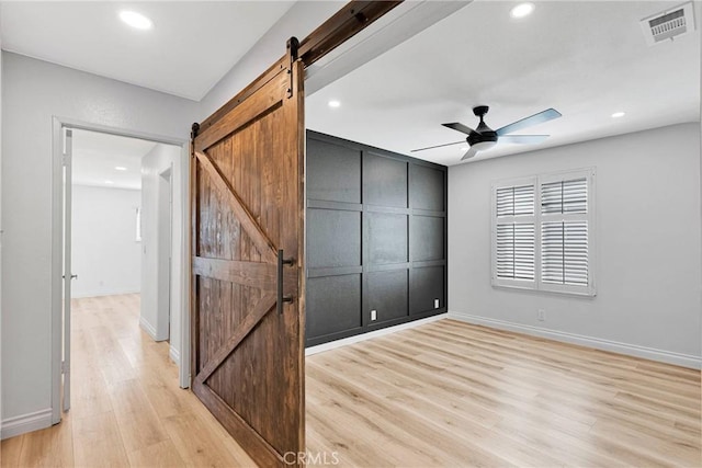 12899 Rain Shadow Rd, Victorville, CA 92395 - unfurnished bedroom with a barn door, light wood-style flooring, recessed lighting, and visible vents