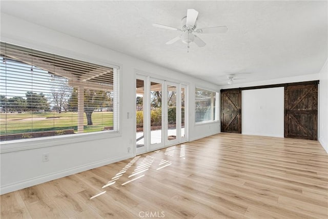 12899 Rain Shadow Rd, Victorville, CA 92395 - unfurnished living room with a ceiling fan, a textured ceiling, a barn door, light wood finished floors, and baseboards