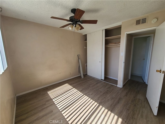 unfurnished bedroom featuring visible vents, a textured ceiling, a closet, and wood finished floors