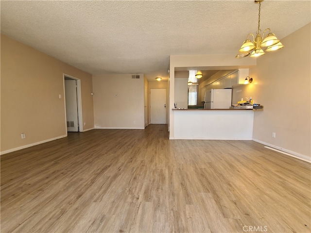 unfurnished living room with a chandelier, visible vents, a textured ceiling, and wood finished floors