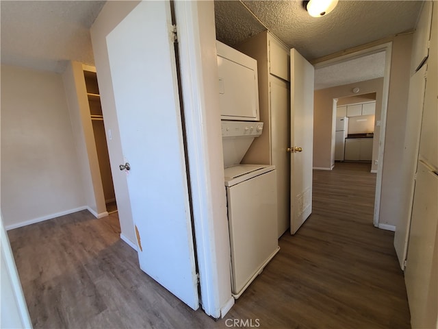 corridor with a textured ceiling, wood finished floors, baseboards, and stacked washing maching and dryer