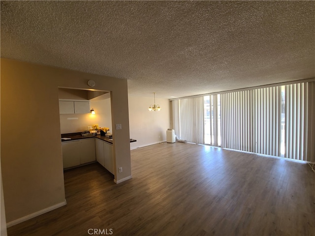 unfurnished living room with baseboards, dark wood-type flooring, an inviting chandelier, and a textured ceiling