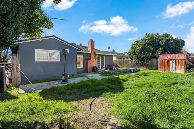 rear view of property featuring a storage unit, stucco siding, an outbuilding, a lawn, and fence