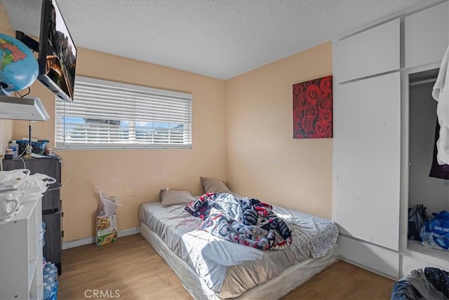 bedroom with wood finished floors, baseboards, and a textured ceiling