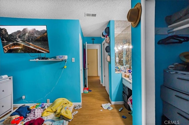 bedroom with visible vents, baseboards, a textured ceiling, and wood finished floors