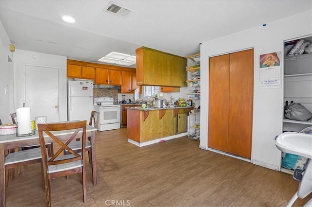 kitchen featuring brown cabinets, white appliances, a peninsula, and wood finished floors