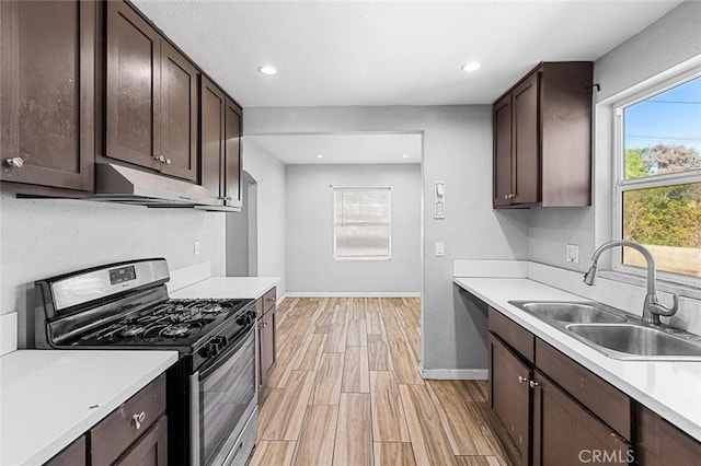 kitchen featuring stainless steel range with gas stovetop, a sink, light countertops, dark brown cabinets, and under cabinet range hood