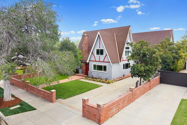 english style home with stucco siding, driveway, a front lawn, fence, and a vegetable garden