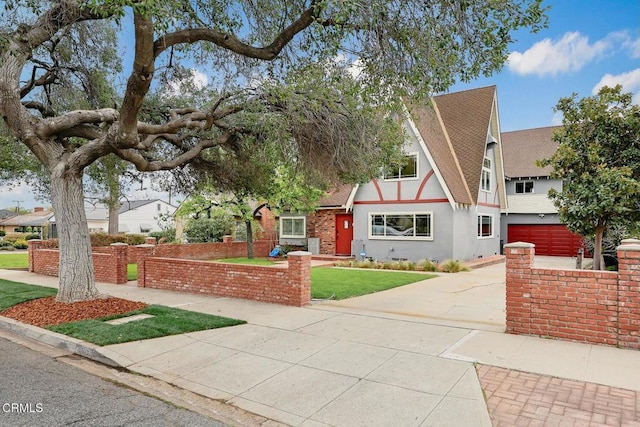 tudor home with a front lawn, roof with shingles, driveway, and stucco siding