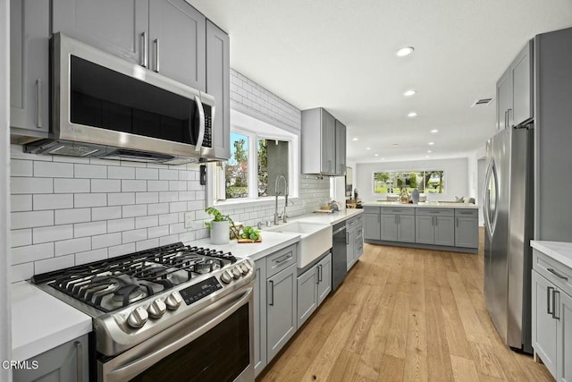 kitchen featuring light wood-style flooring, a sink, gray cabinetry, light countertops, and stainless steel appliances