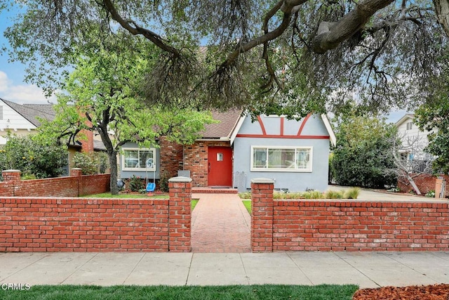 tudor house with stucco siding, a shingled roof, and fence