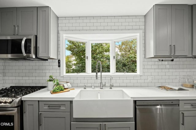 kitchen with backsplash, appliances with stainless steel finishes, gray cabinetry, and a sink