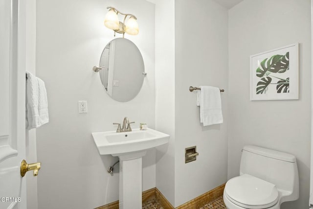 half bath featuring toilet, baseboards, and a sink