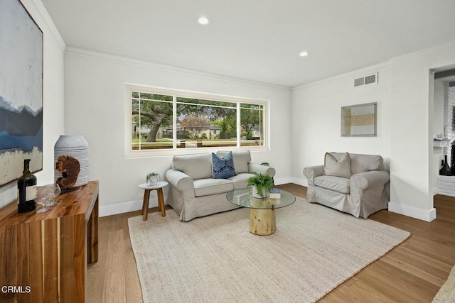 living area with wood finished floors, baseboards, visible vents, recessed lighting, and ornamental molding